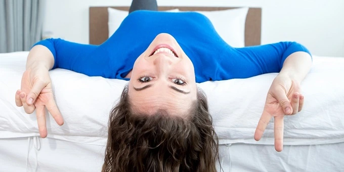fiatal lány kék pizsamában hanyat fekszik az ágy szélén